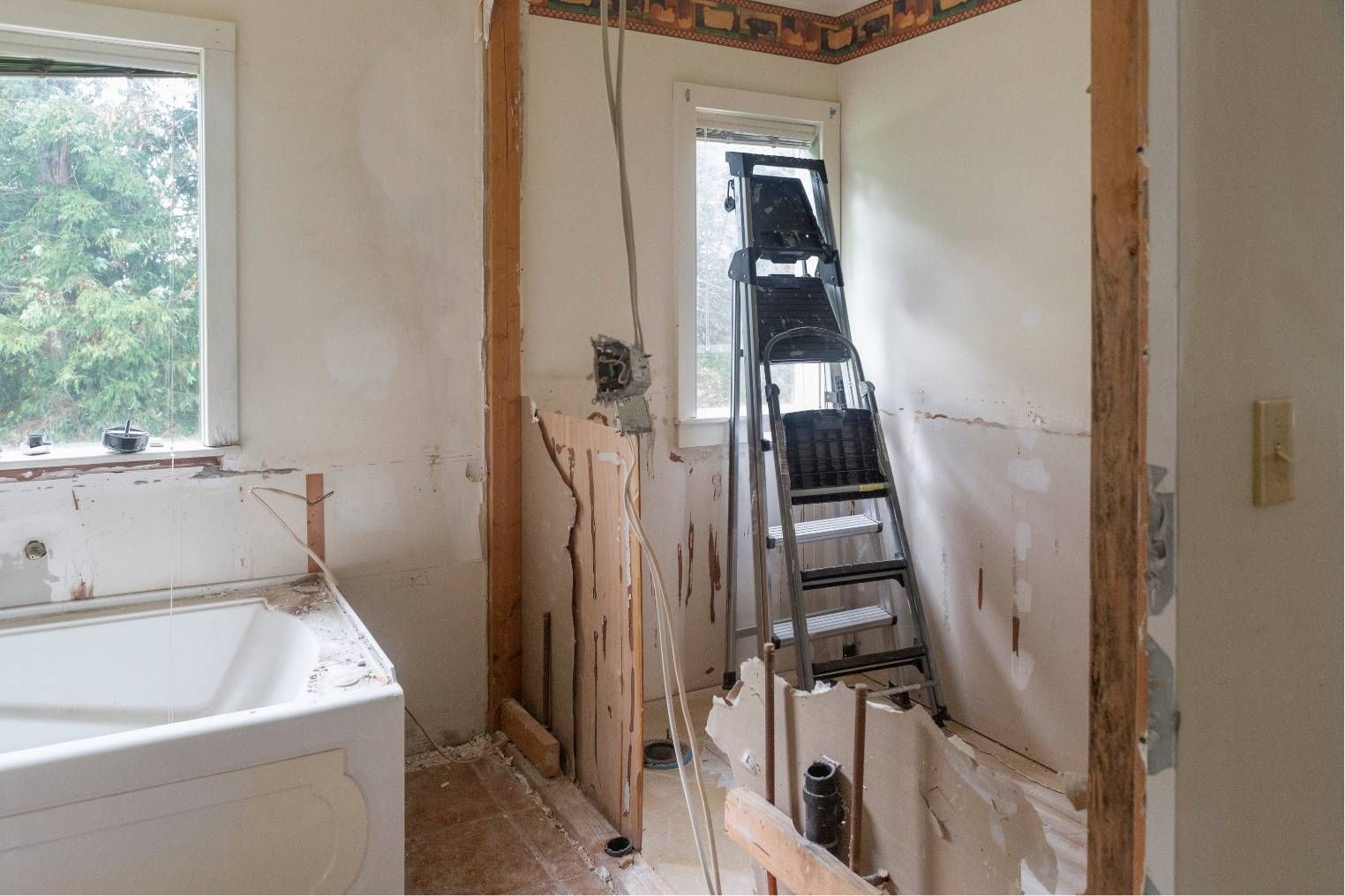 Bathroom under renovation with a ladder, exposed wiring, and a partially stripped wall.