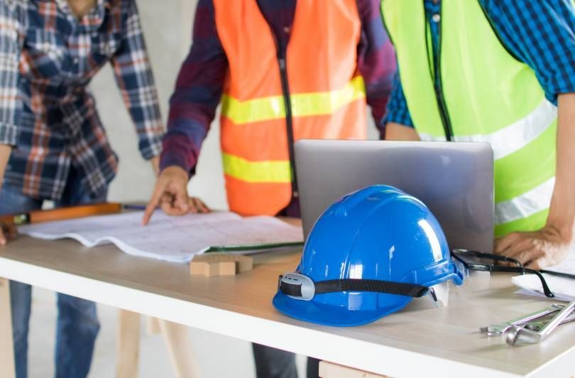 Construction team reviewing plans at a table with a blue hard hat and laptop
