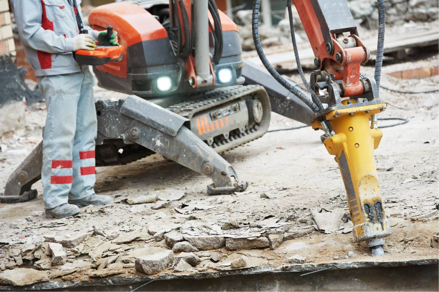 Workers using a jackhammer and excavator to break up concrete at a construction site
