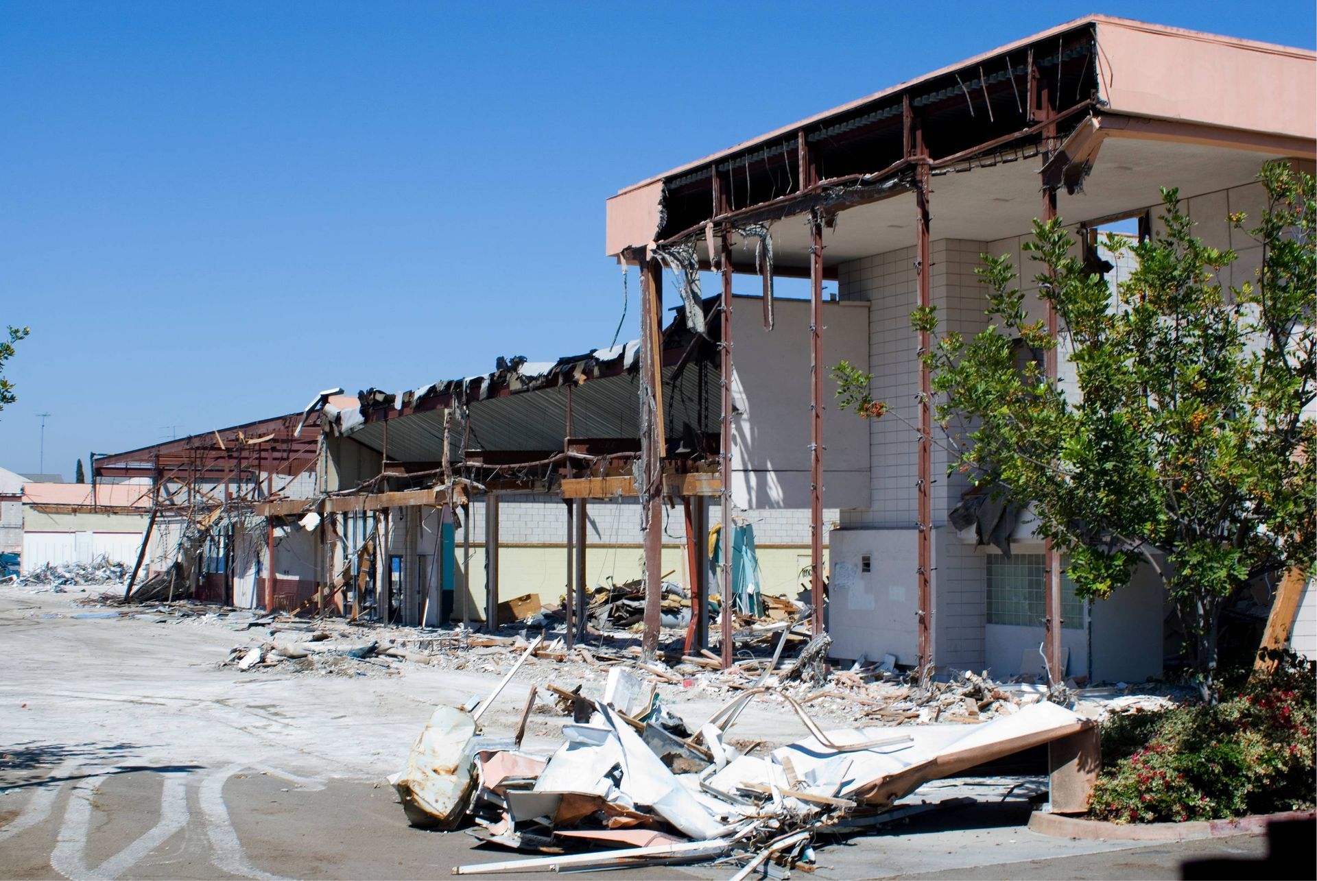 Severely damaged building with collapsed roof and debris scattered outside under a clear blue sky