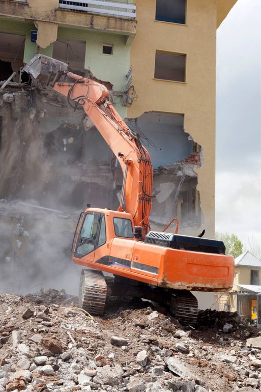 Orange excavator demolishing a building amid rubble and dust