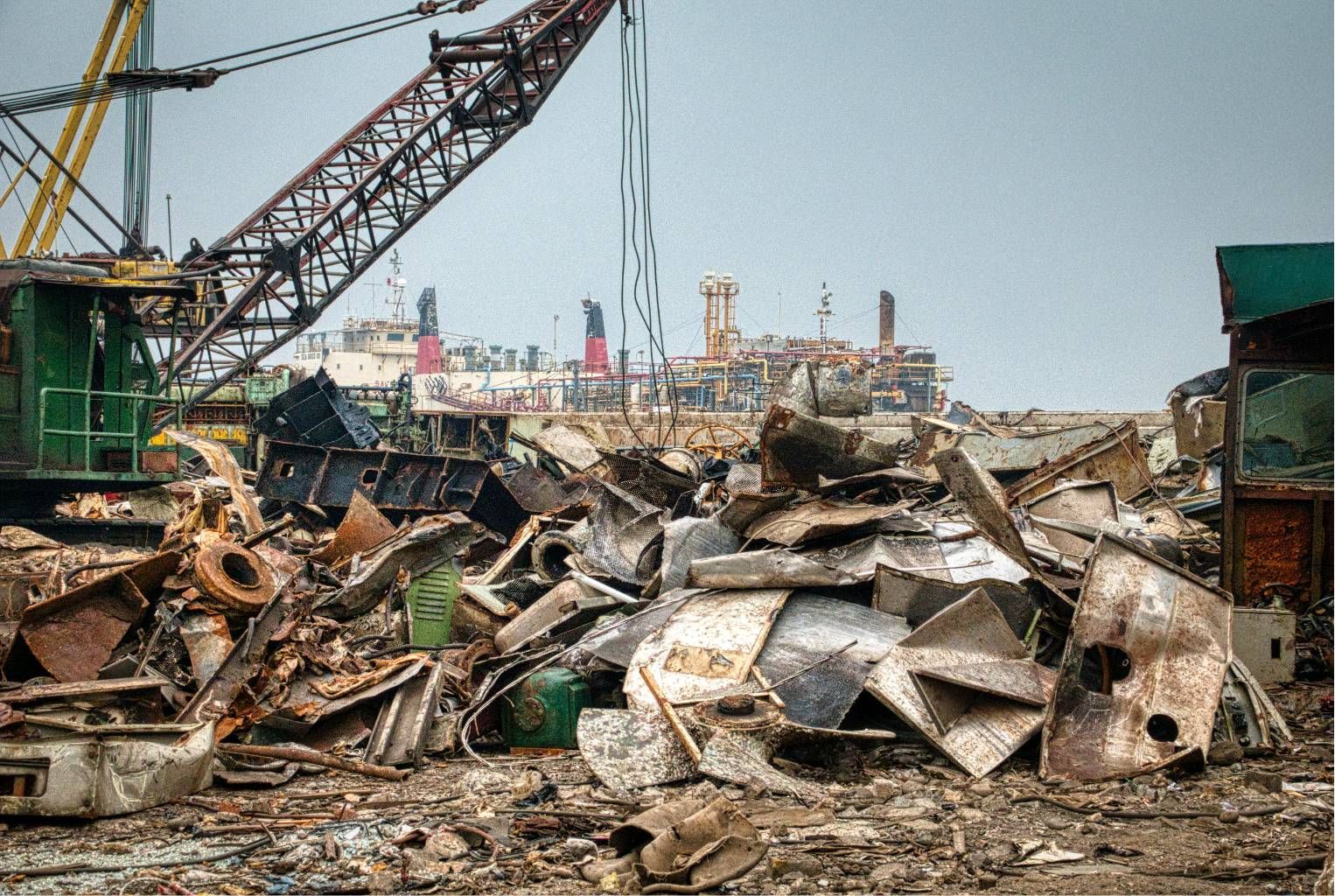 Scrap yard with piles of crushed metal and a large crane under an overcast sky