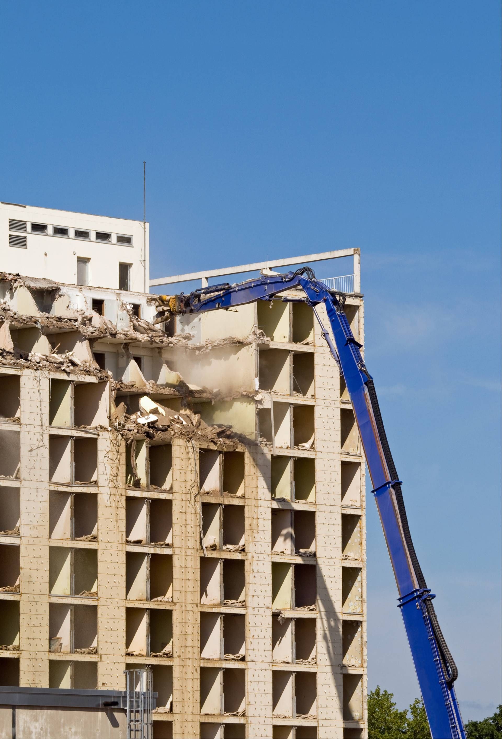 Demolition crane tearing down a beige building under a clear blue sky