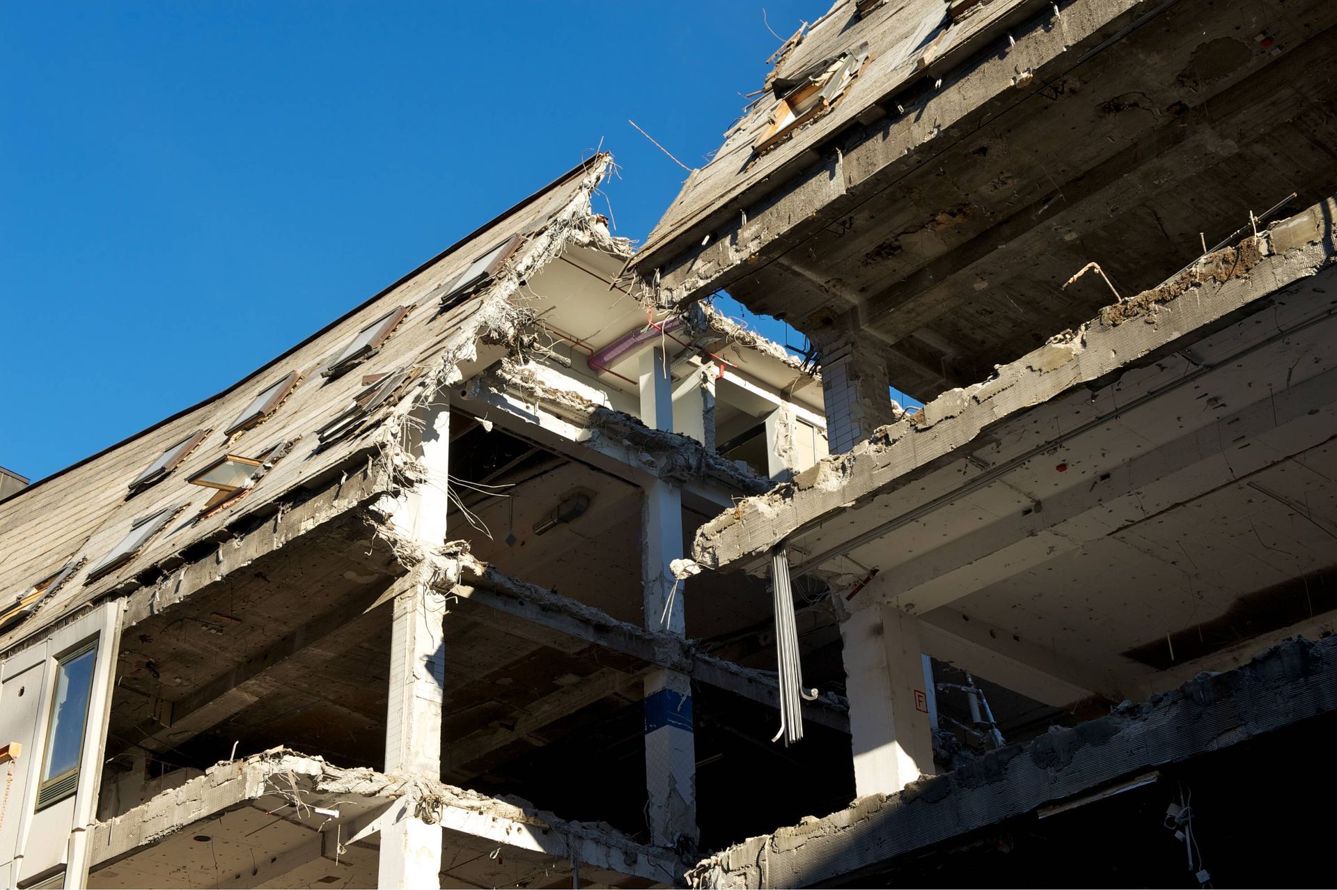 Partially collapsed concrete building with exposed floors and rubble against a blue sky