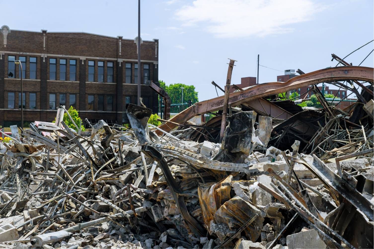 Collapsed building rubble beside a brick school building under a clear sky