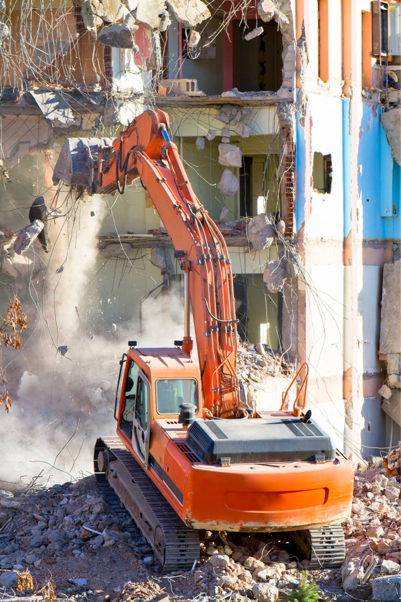 Orange excavator demolishing a building wall amid rubble and dust