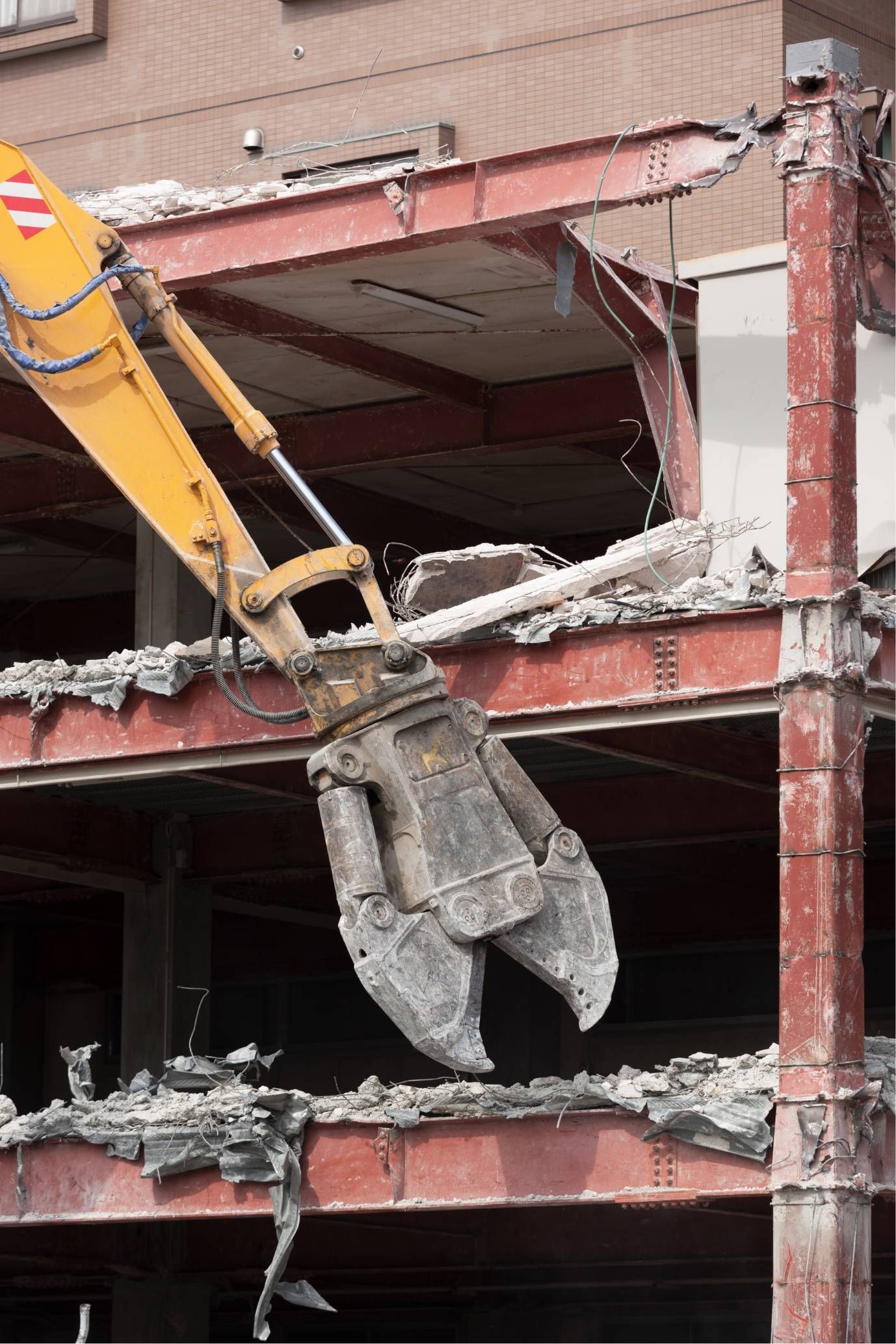 Excavator arm with concrete crusher demolishing a multi-story building