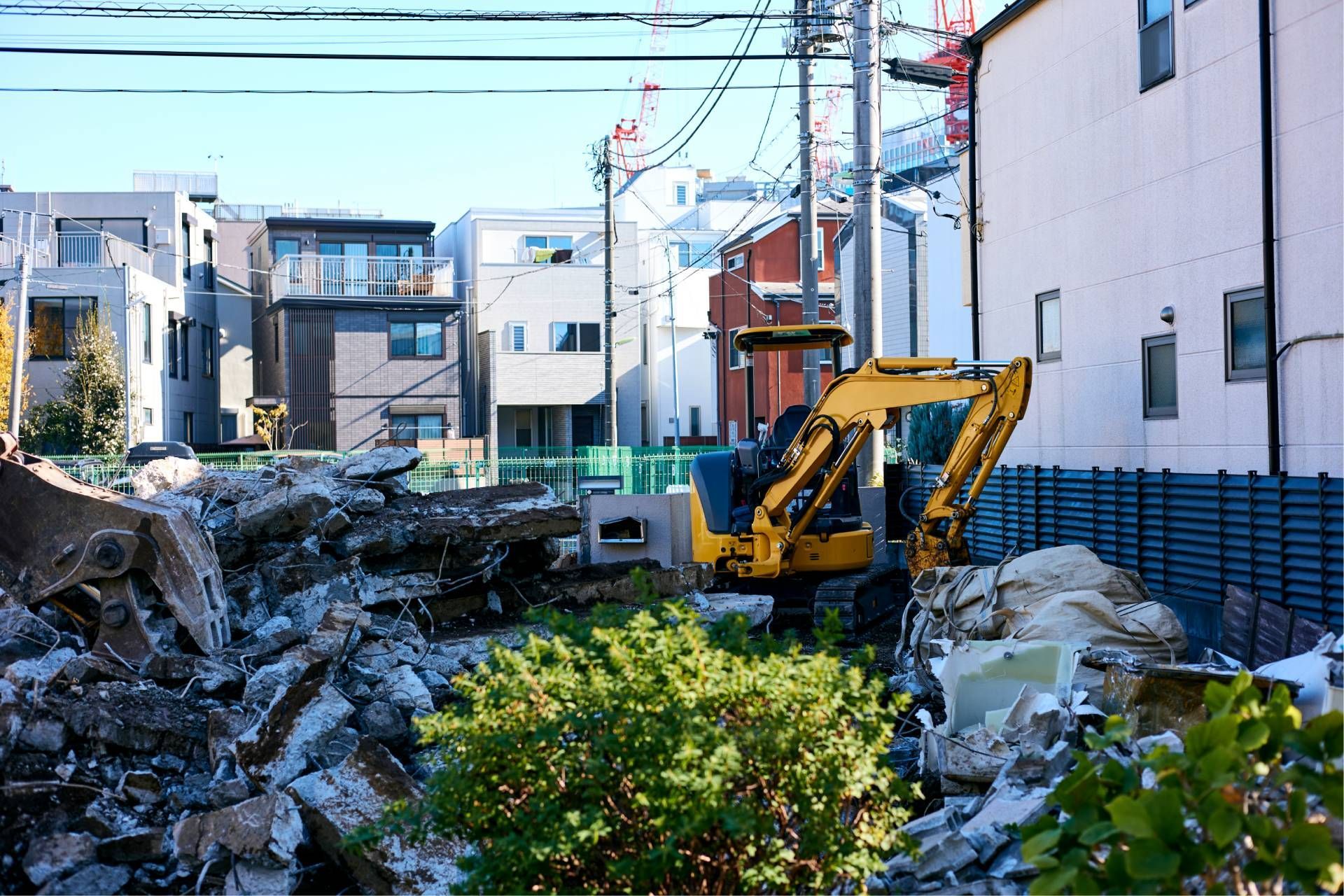 Yellow excavator clearing rubble in a narrow residential street with damaged buildings nearby