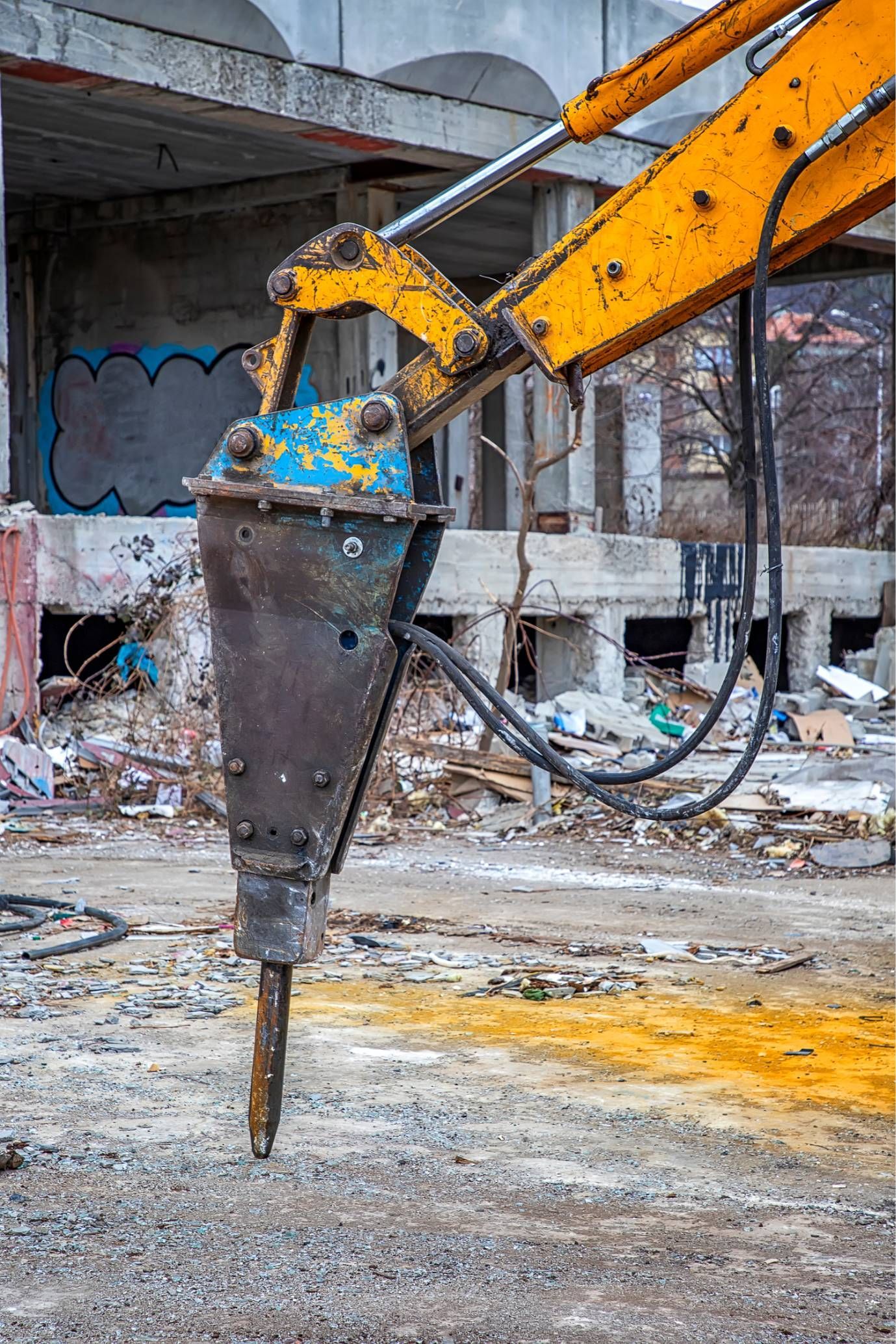 Yellow excavator breaking concrete in a rubble-filled demolition site