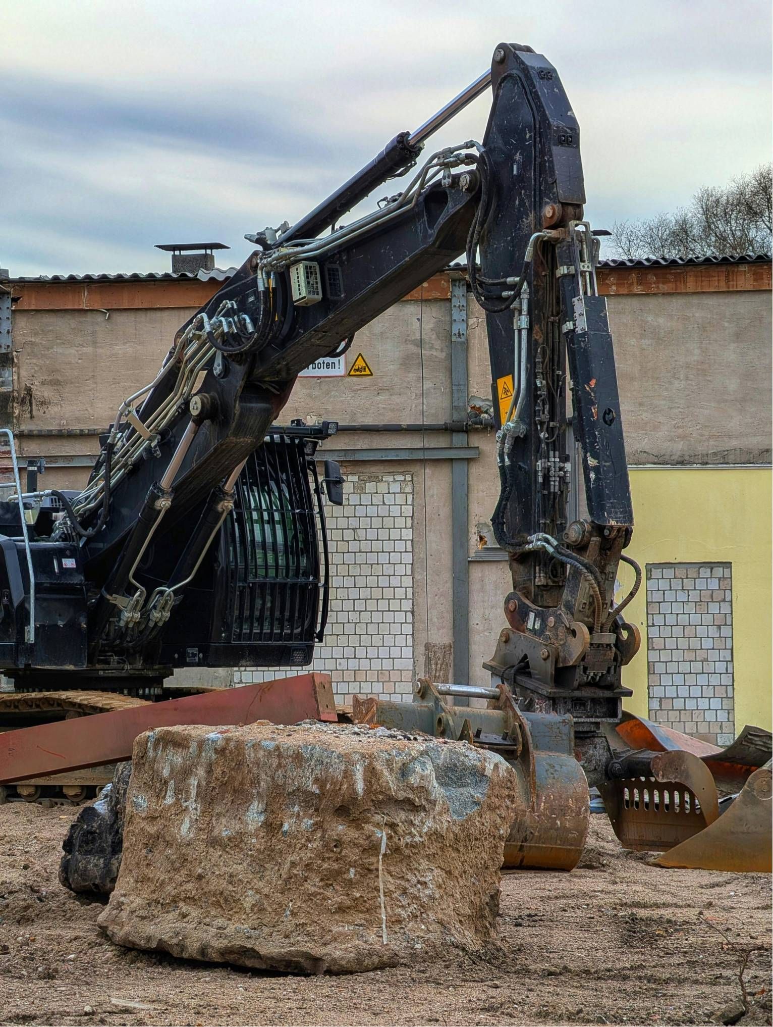 Large excavator beside a rough stone block in a construction yard