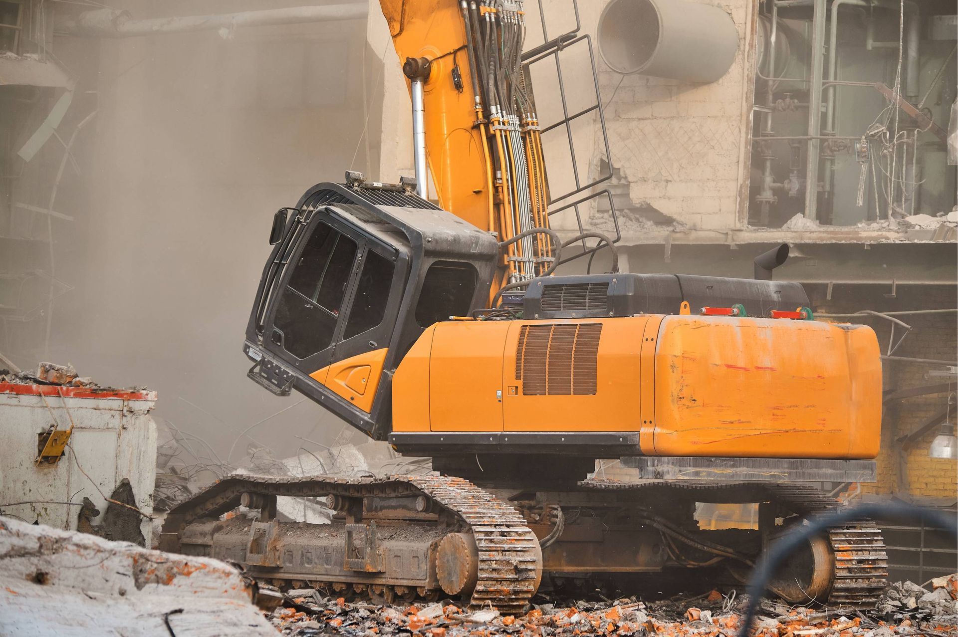 Orange excavator amid rubble at a demolition site, its cab tilted and dust filling the air.