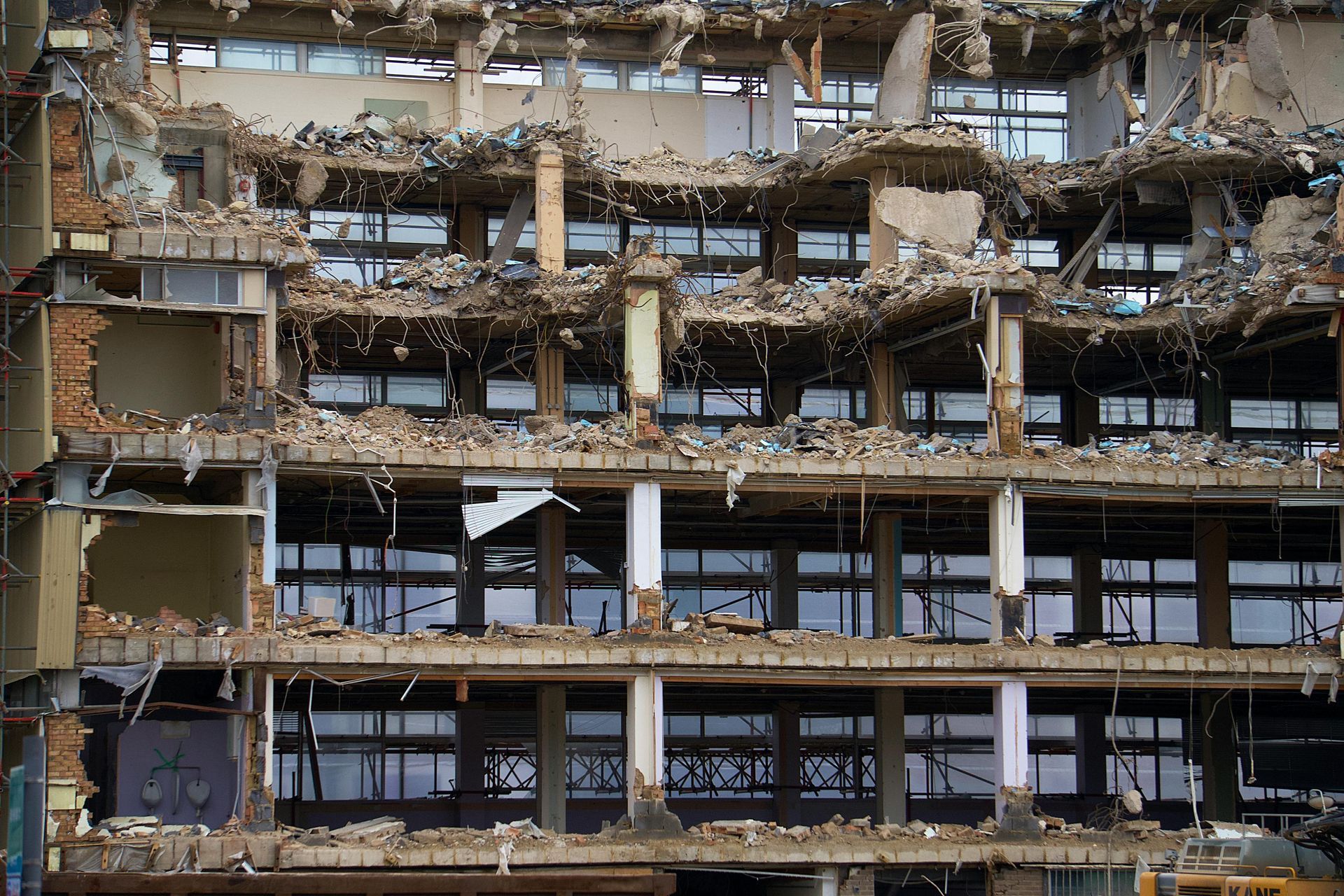 Collapsed building facade with exposed floors, broken windows, and heavy rubble debris.