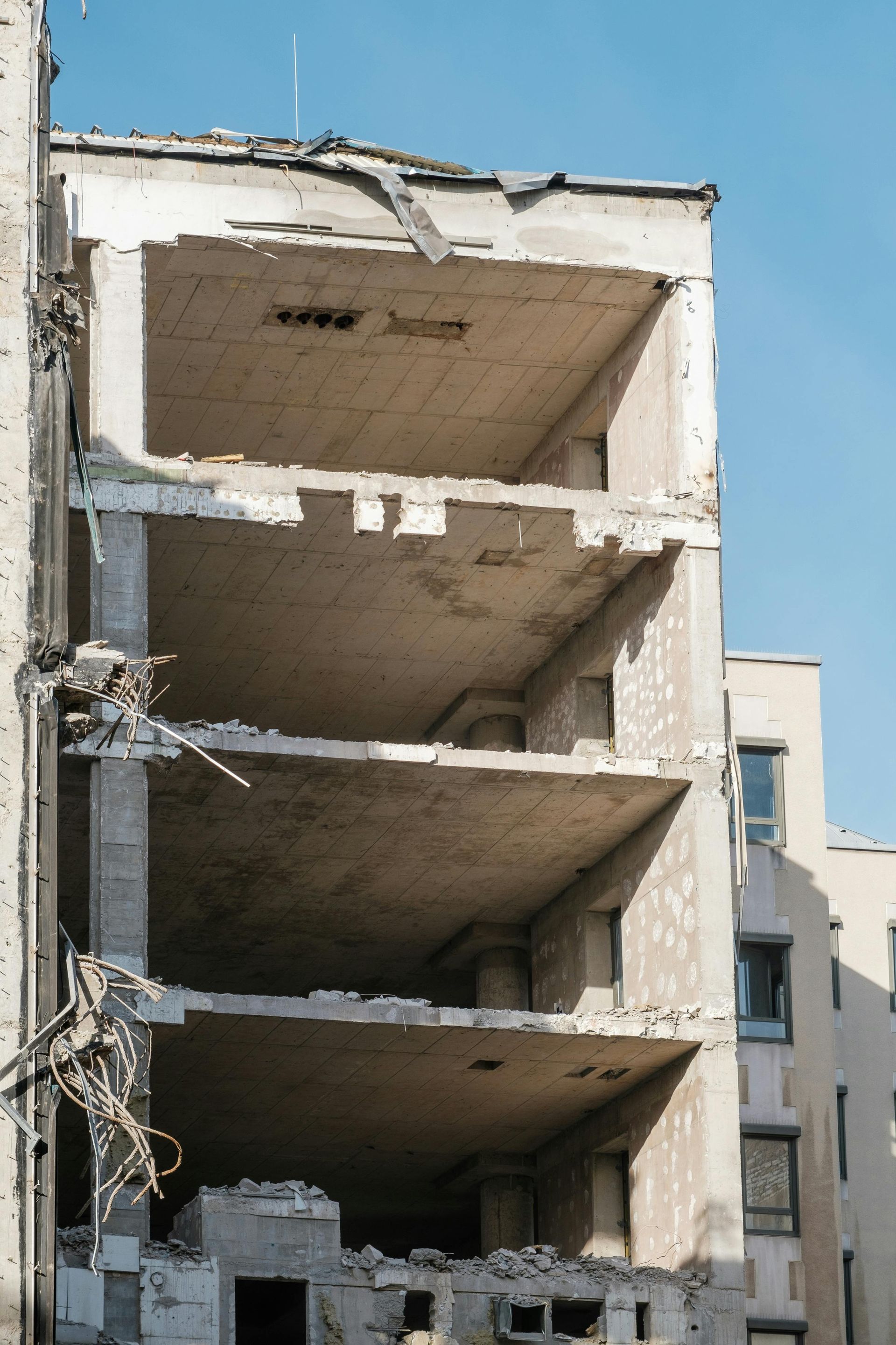 Damaged multi-story building with exposed concrete floors and a partially collapsed facade against a blue sky