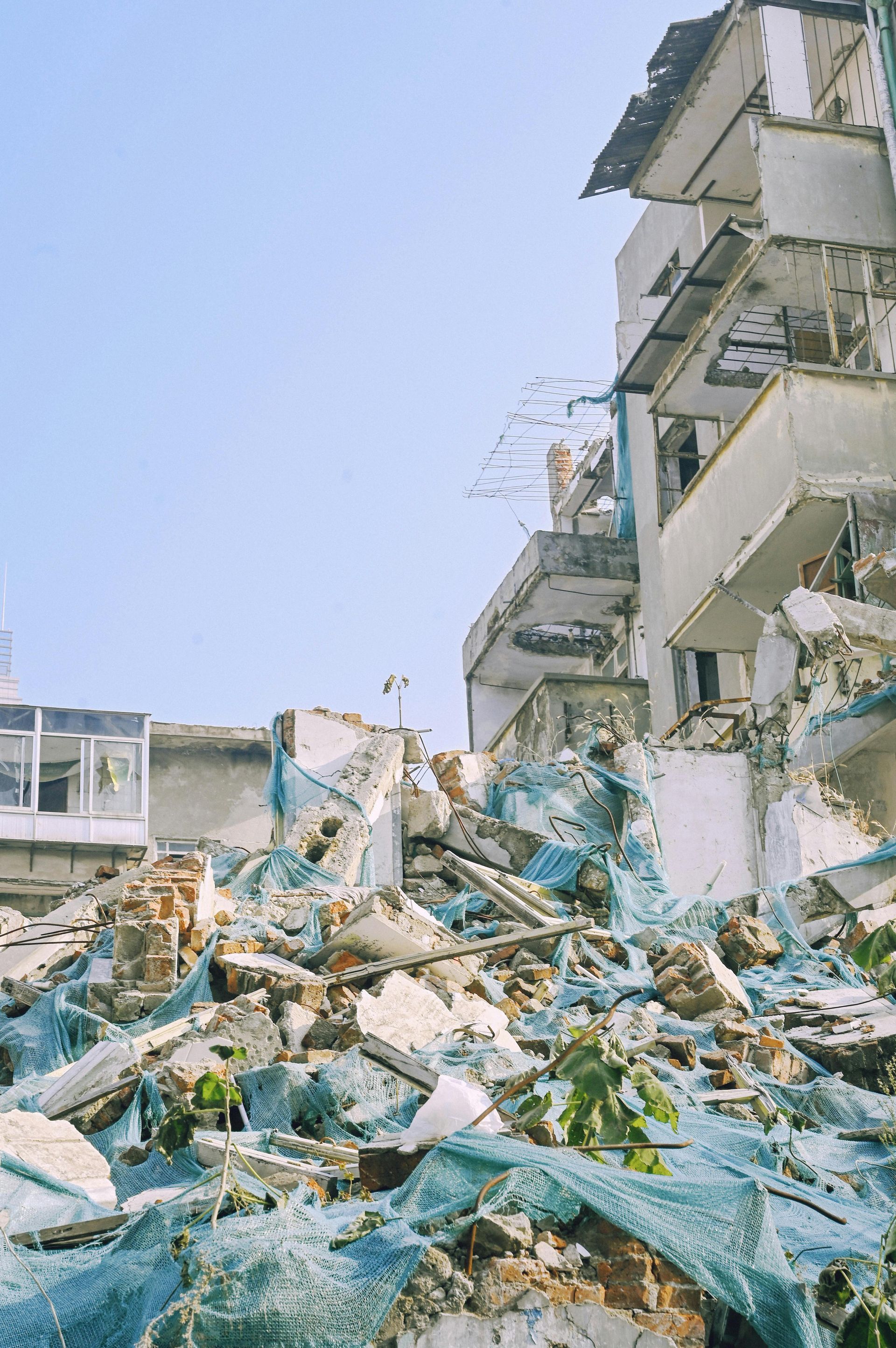 Collapsed building rubble beside a partially standing apartment block under a clear sky