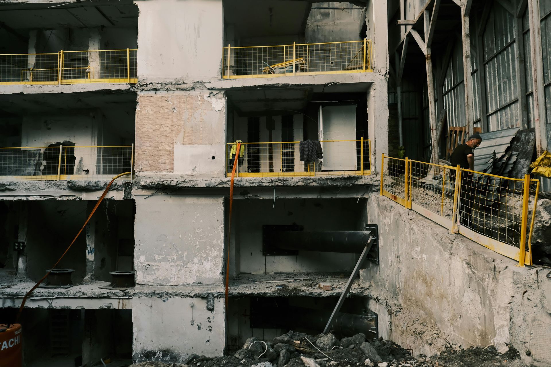 Partially demolished concrete building interior with exposed floors, yellow safety railings, and rubble below