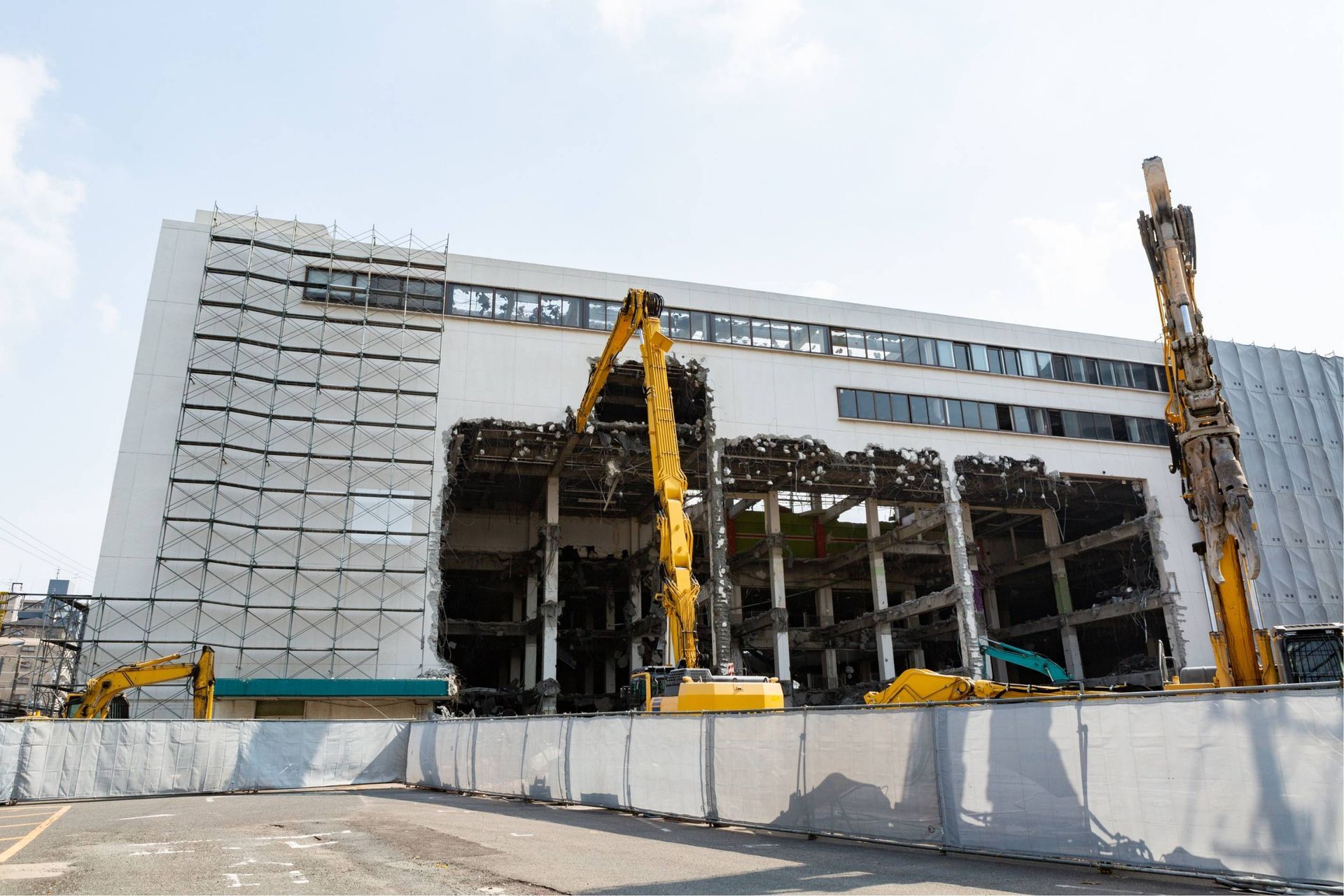 Partially built multi-story building with cranes and scaffolding behind a construction barrier