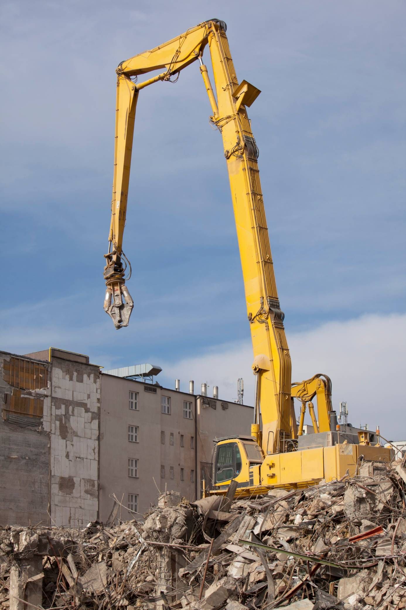Yellow excavator demolishing a building, with rubble in the foreground.
