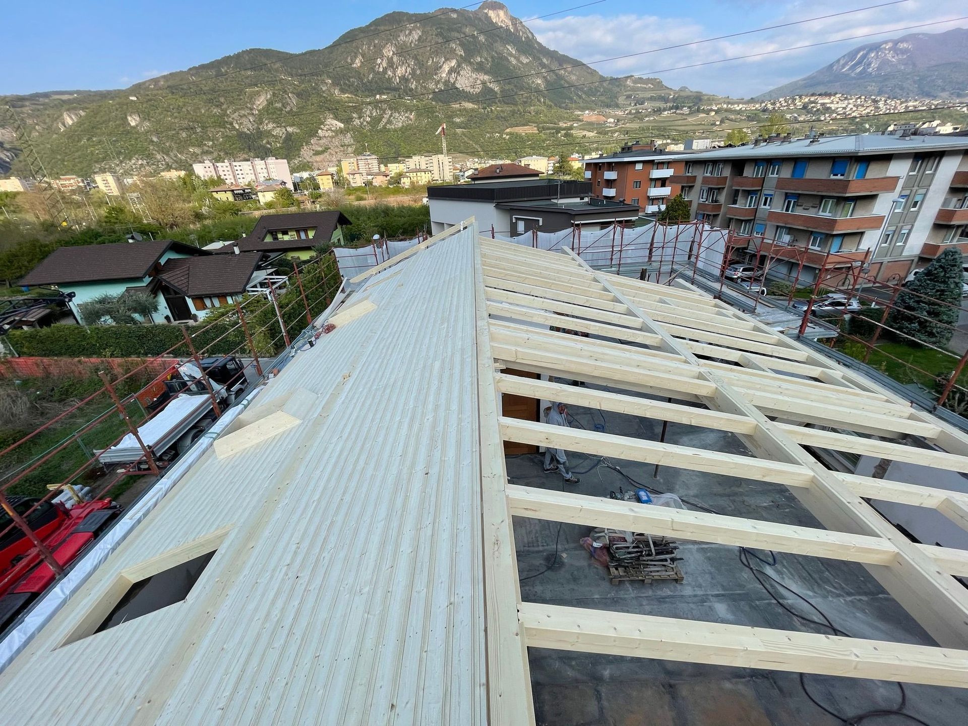Vista dall'alto del tetto di un edificio in costruzione, che mostra i pannelli bianchi già rifiniti sulla sinistra e le travi in legno a vista.