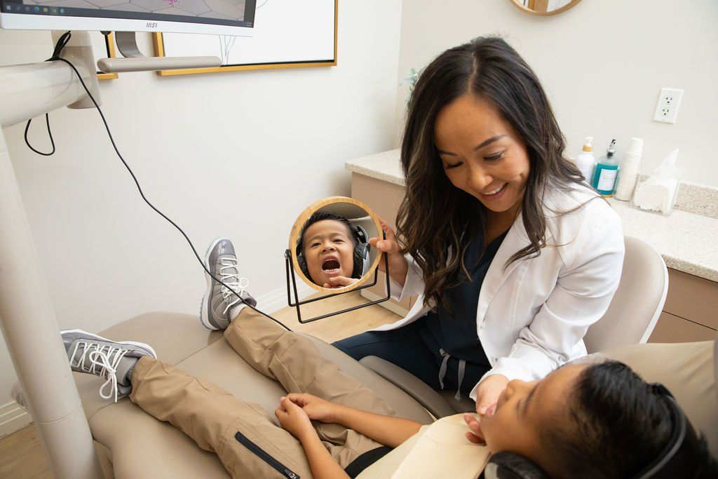 A woman is looking at a child 's teeth in a mirror.