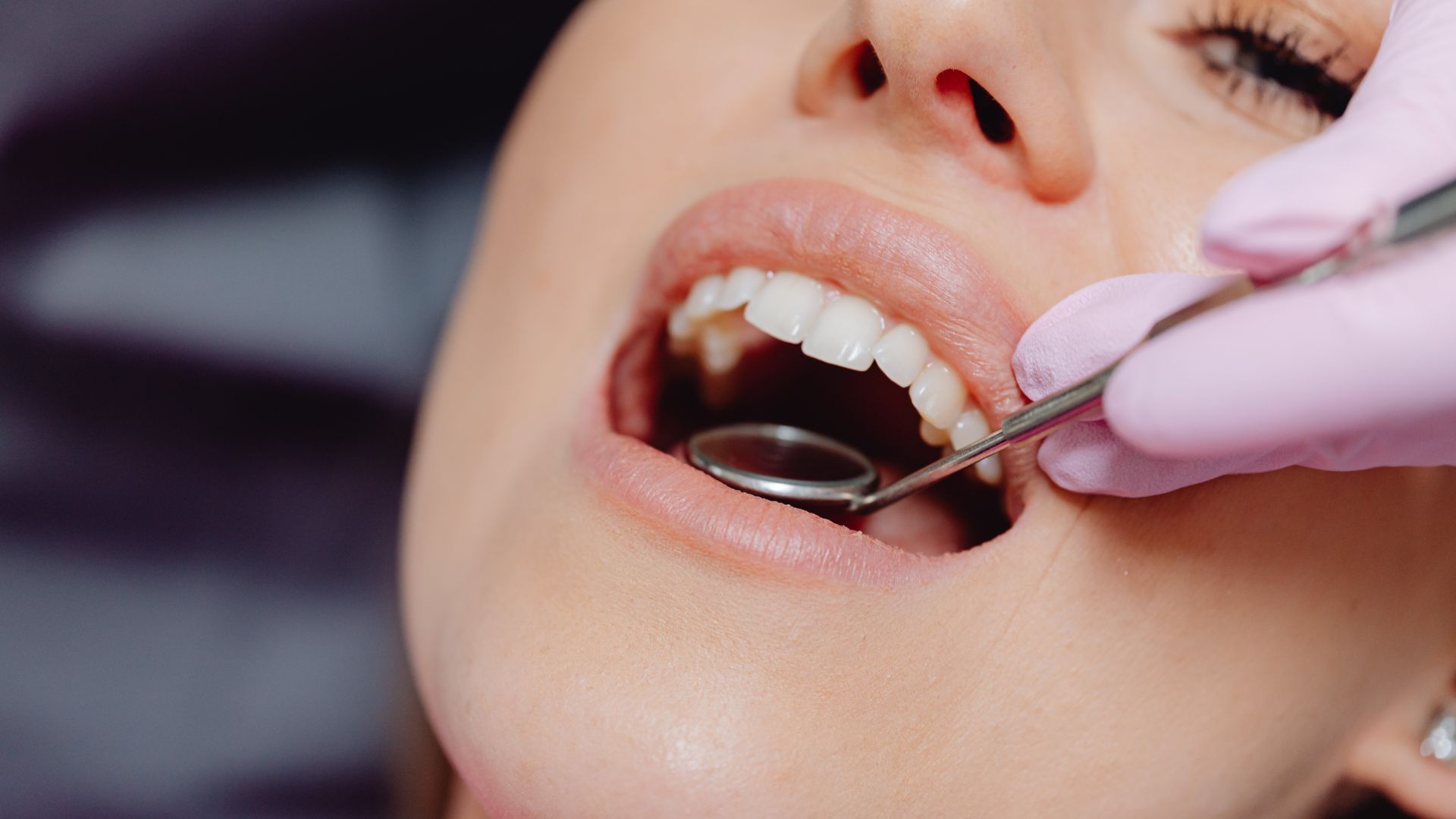 Dentist examining a patient’s open mouth with a mirror and probe.