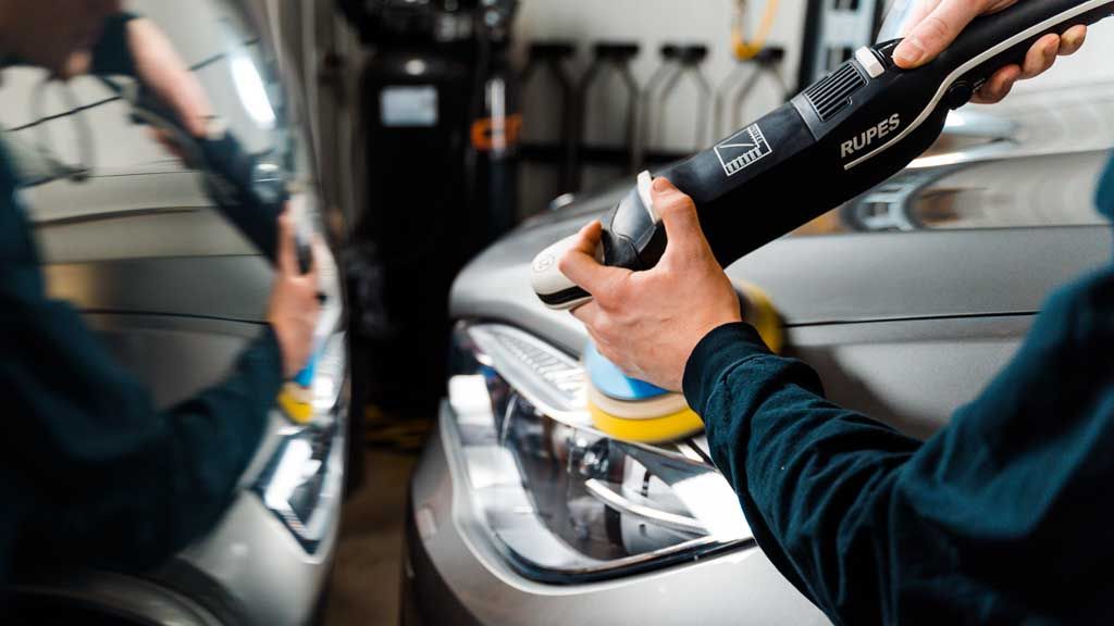 A man is polishing the headlights of a car with a machine.