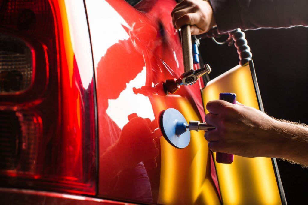 A person is using a hammer to fix a dent on a red car.