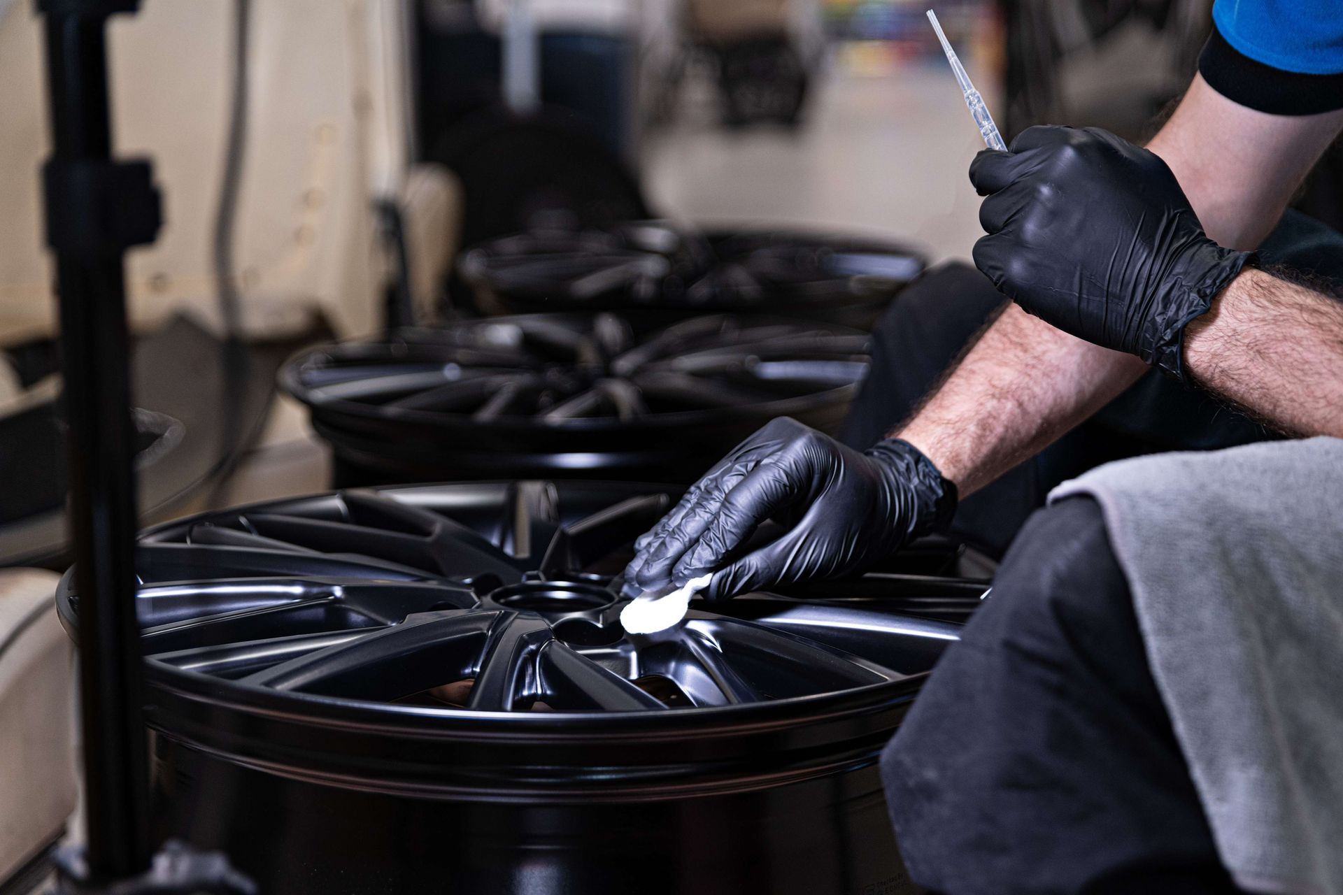 A man wearing black gloves is polishing a wheel in a garage.