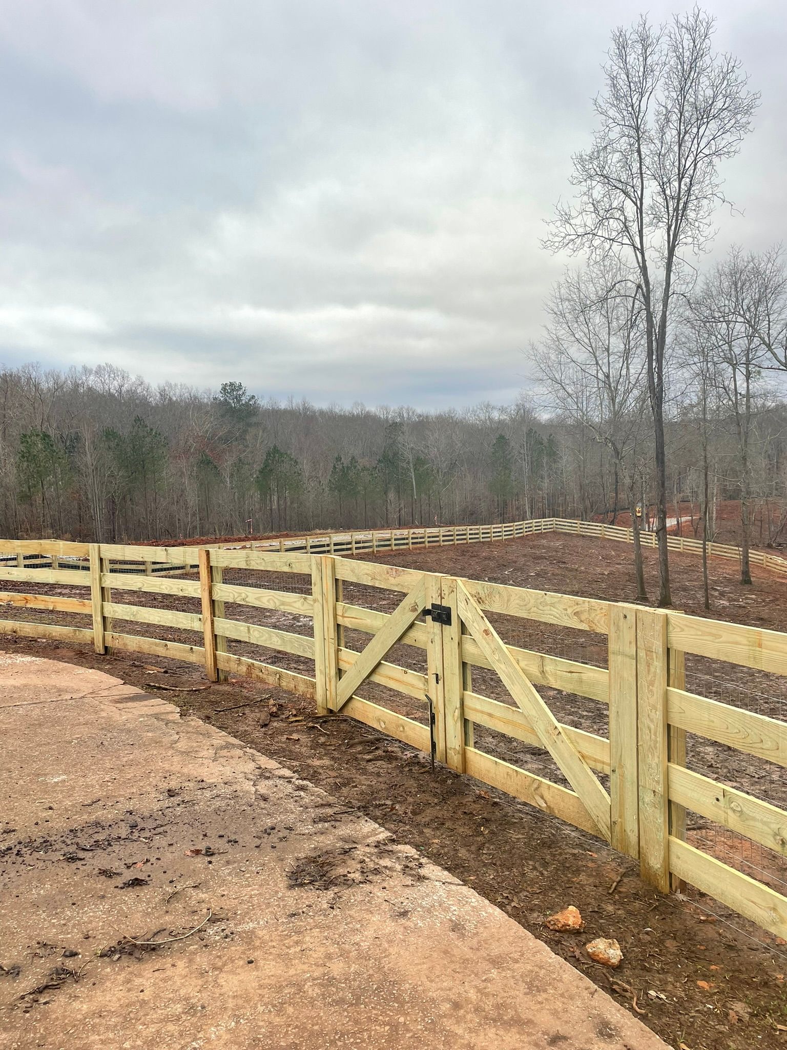A wooden fence with a gate in the middle of a dirt road.