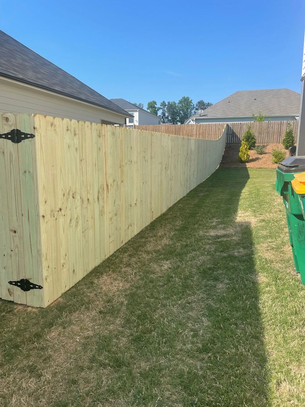 A wooden privacy fence is sitting in the grass in front of a house.
