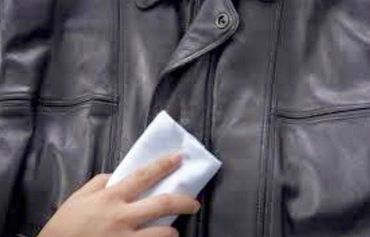 Una mano che infila un foglio di carta bianco piegato nella tasca interna di una giacca di pelle nera