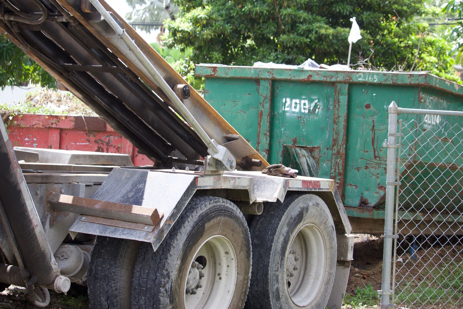 Truck lifting a rusty green dumpster. Wheels and silver frame.