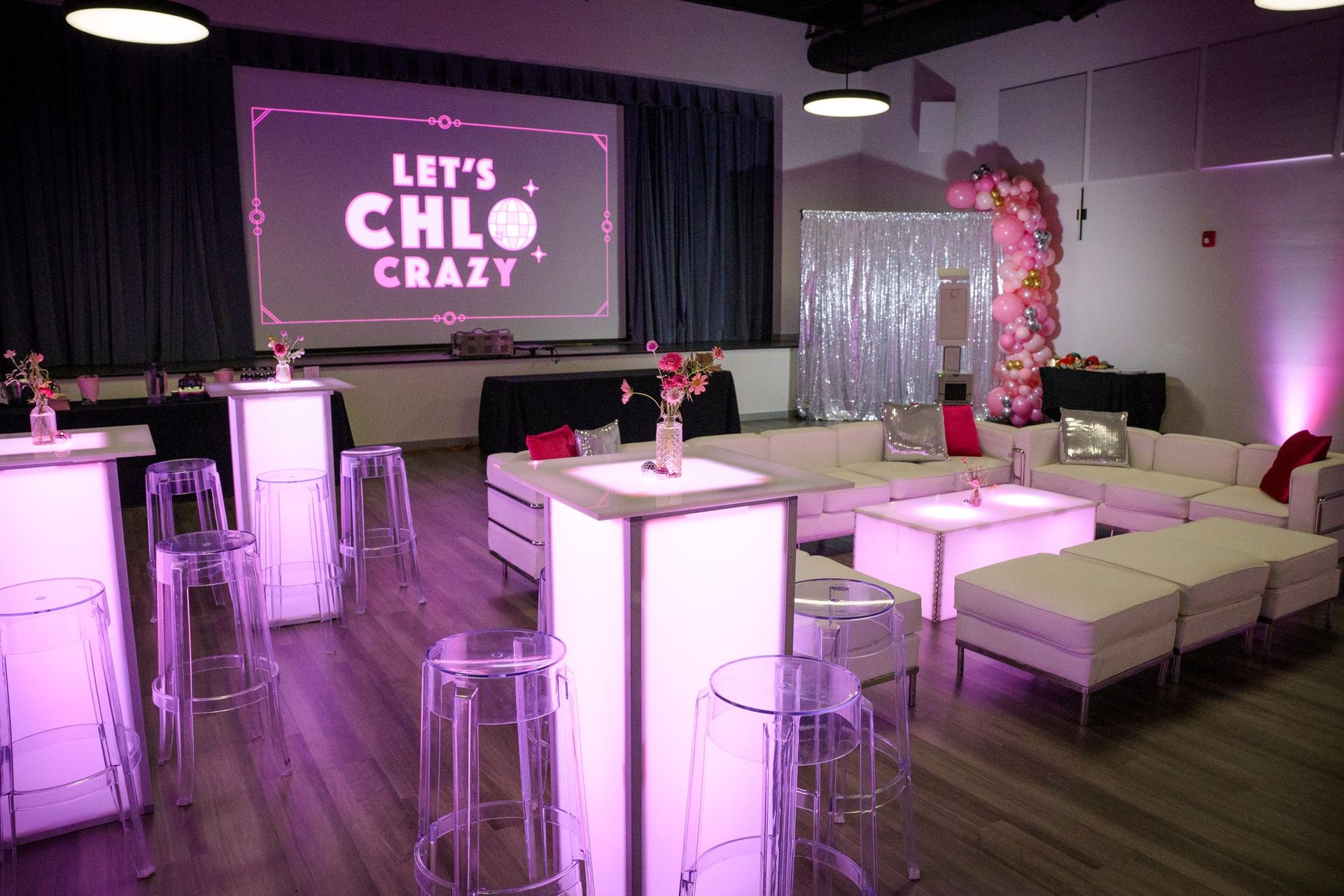 Party venue with white seating, transparent chairs, and a screen that says 