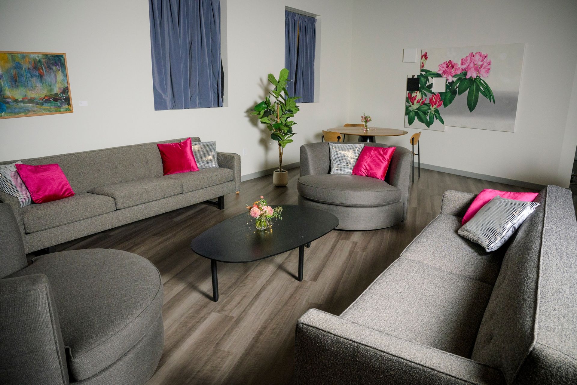 Living room with gray sofas, pink pillows, black coffee table, artwork, and wood floors.