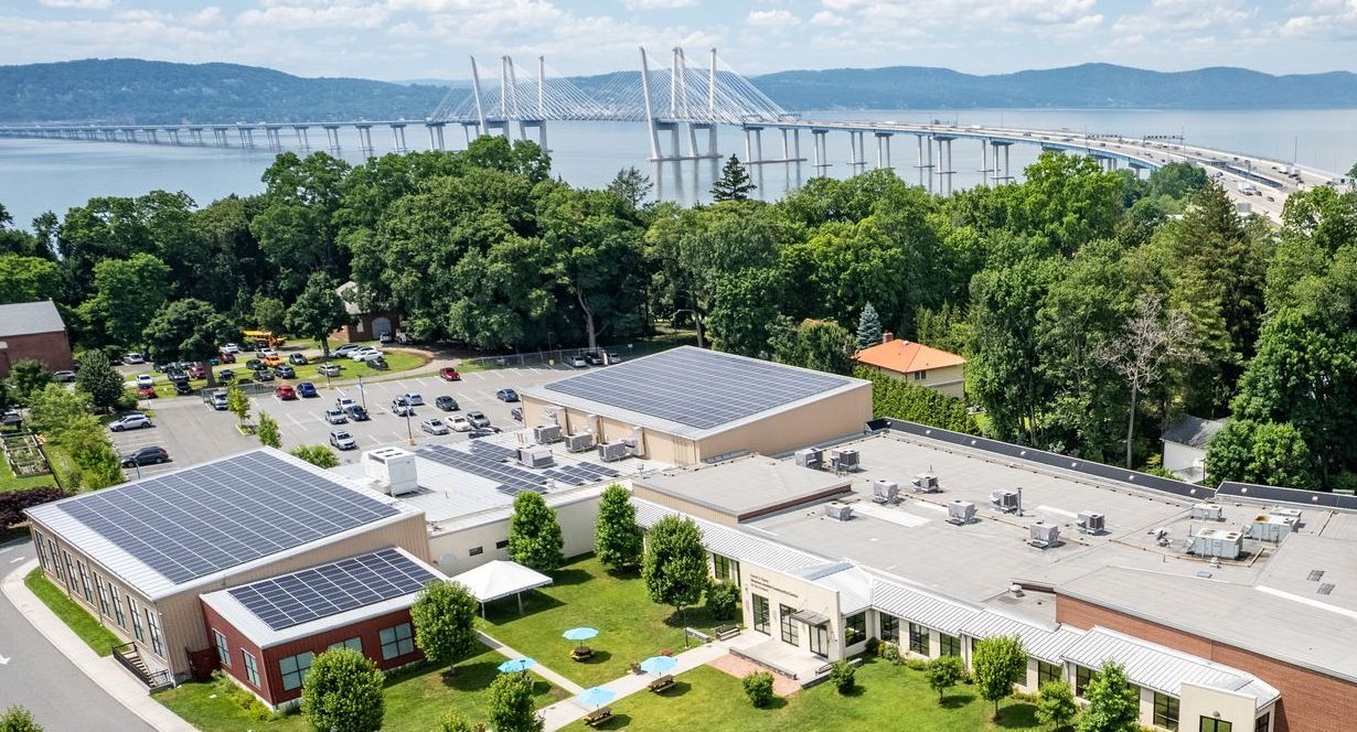 Buildings with solar panels on roofs, green lawns, and a large bridge in the background.