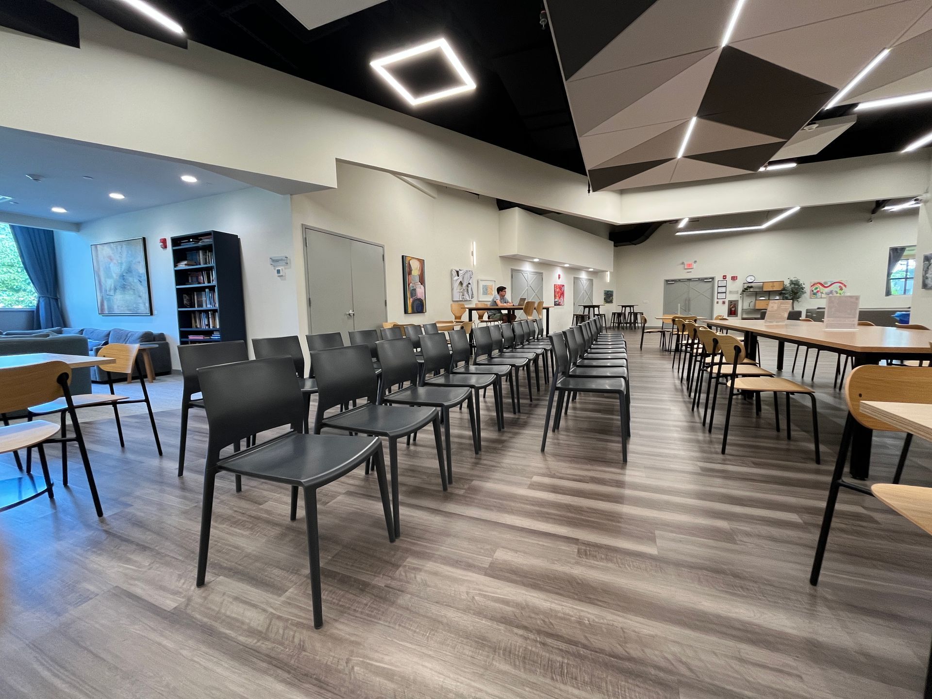 An empty event space with rows of chairs, tables, bookshelves and art.