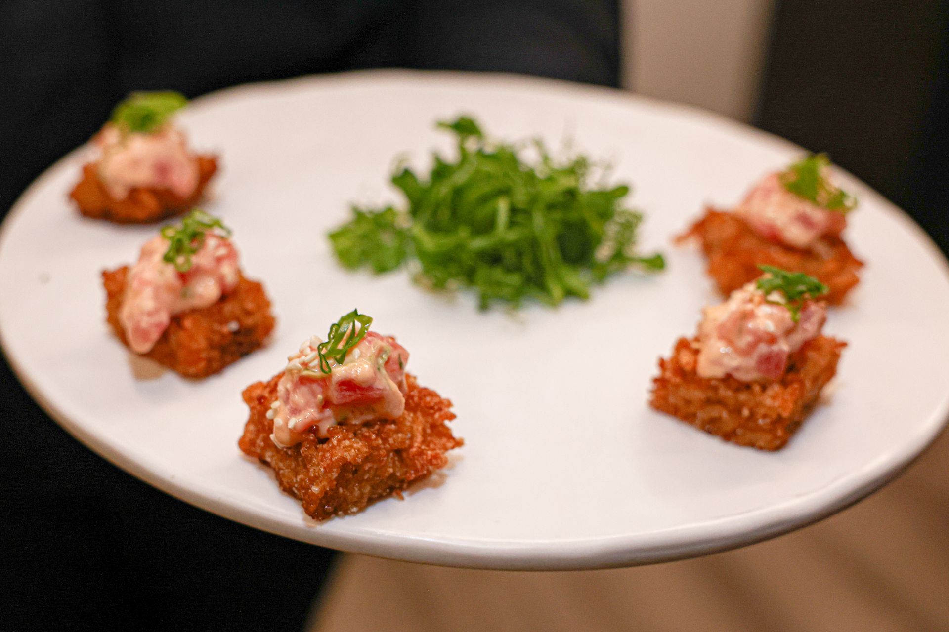Plate of fried square appetizers topped with pink food and green garnish.
