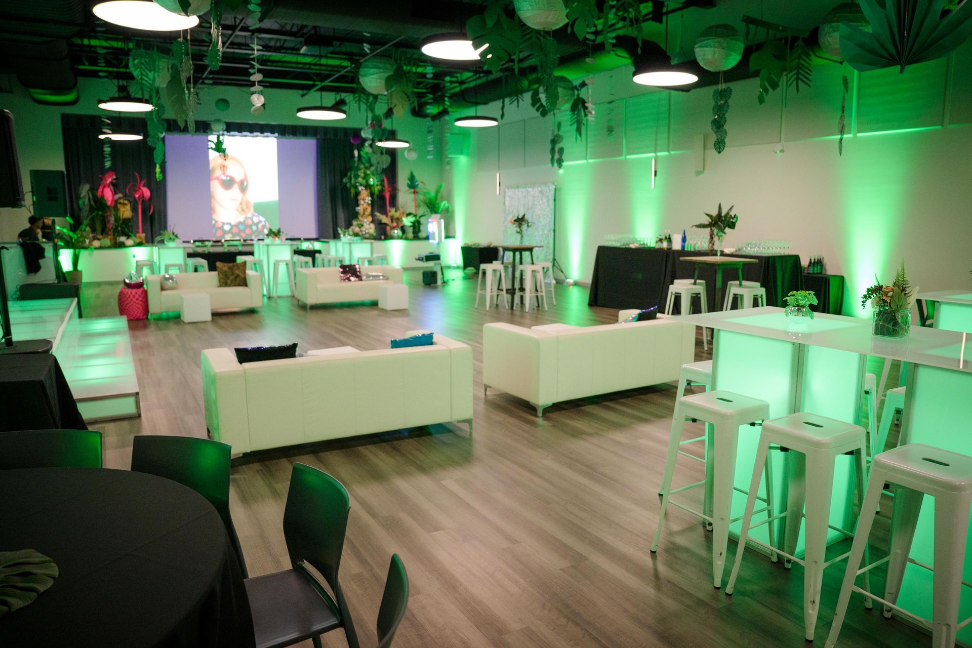 Event space with white furniture and green lighting; a screen in the background.