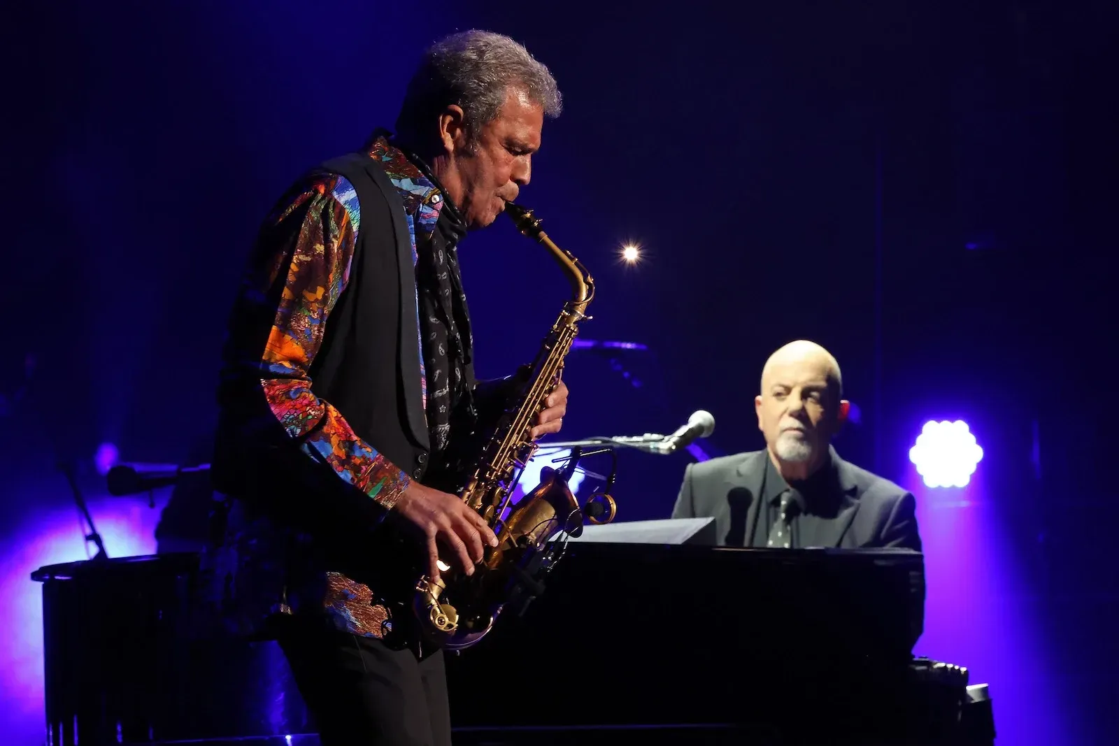 Saxophonist and pianist performing onstage under purple lights