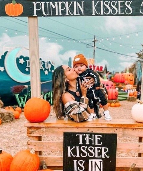 Woman and child on pumpkin-themed bench at fall festival, surrounded by pumpkins and autumn decor