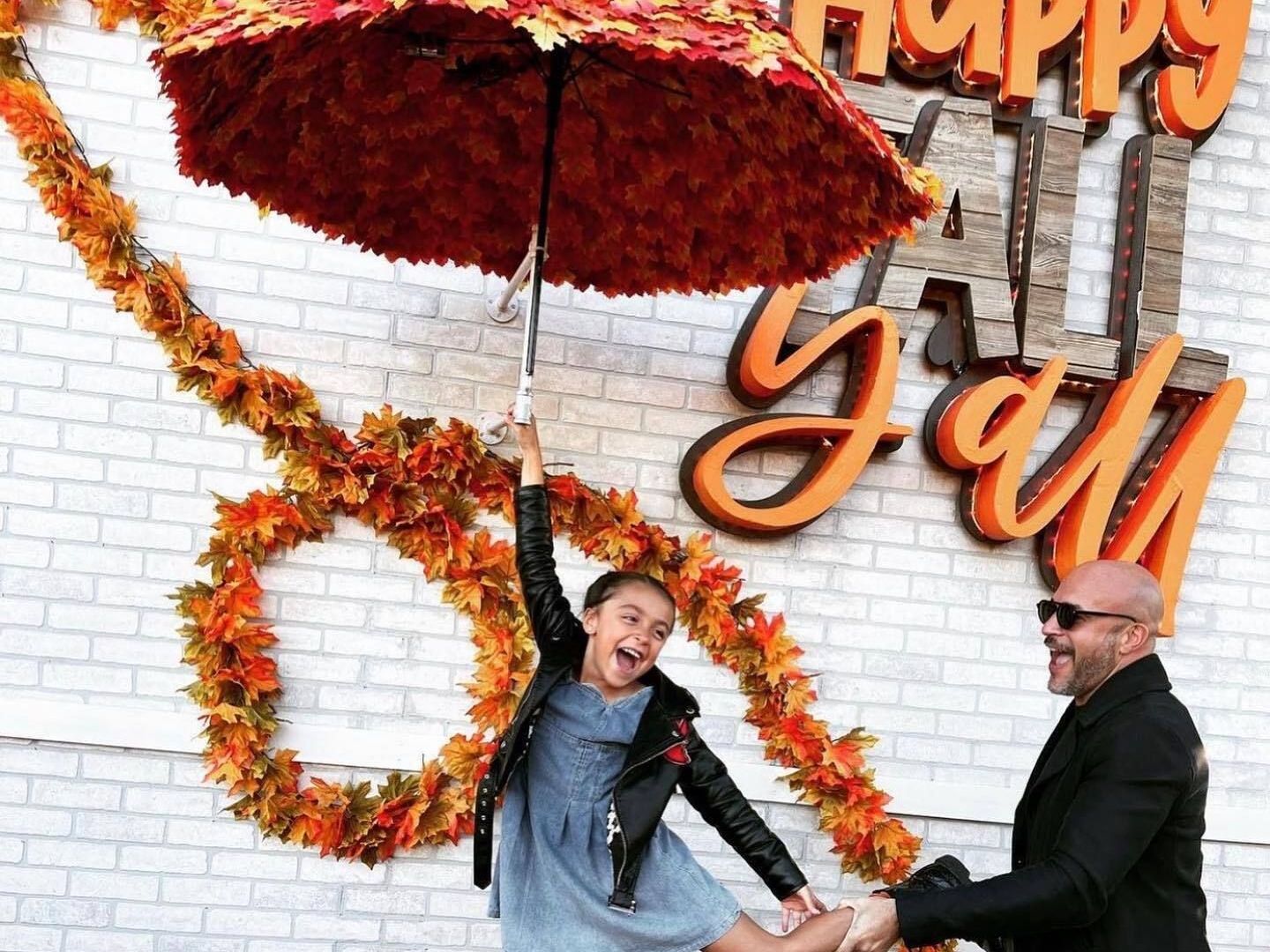 Person holding a red umbrella in front of a “Happy Fall” autumn display