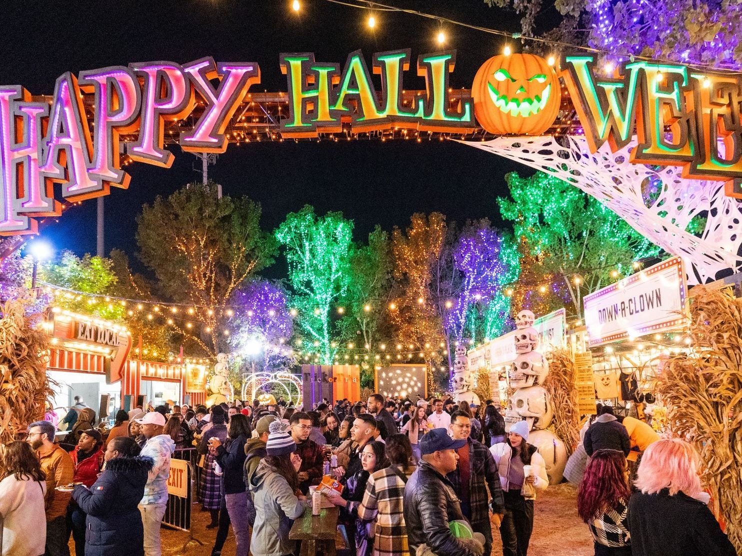 Crowd under a colorful “Happy Halloween” arch at a festive nighttime event with glowing decorations