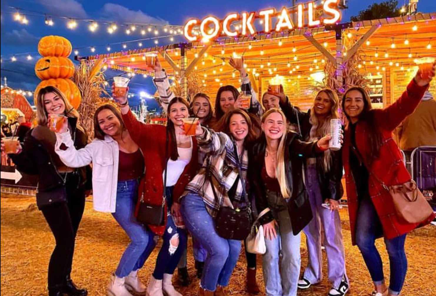 Group of friends posing and cheering under string lights at an outdoor cocktail event.