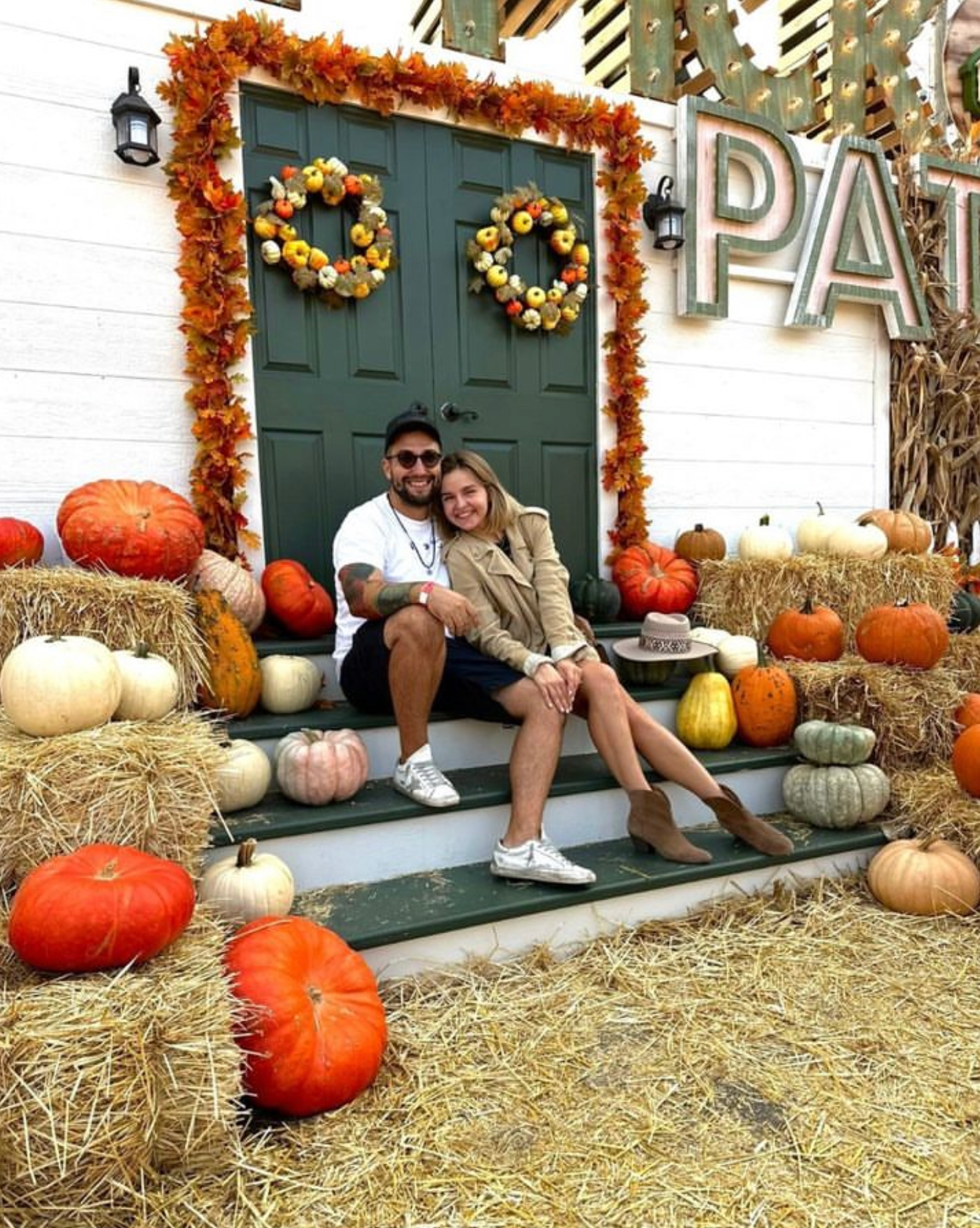 Couple sitting on steps in front of a fall-decorated door with pumpkins and autumn wreaths