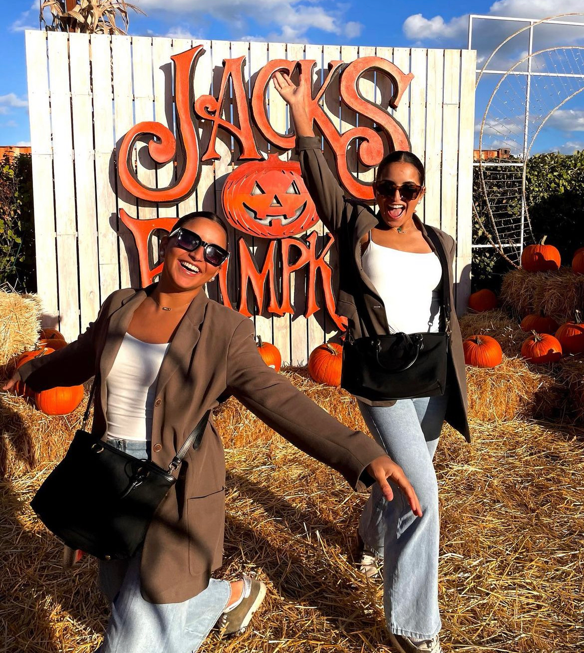 Two people posing at a pumpkin patch with a “Jacks Pumpkin” sign and hay bales
