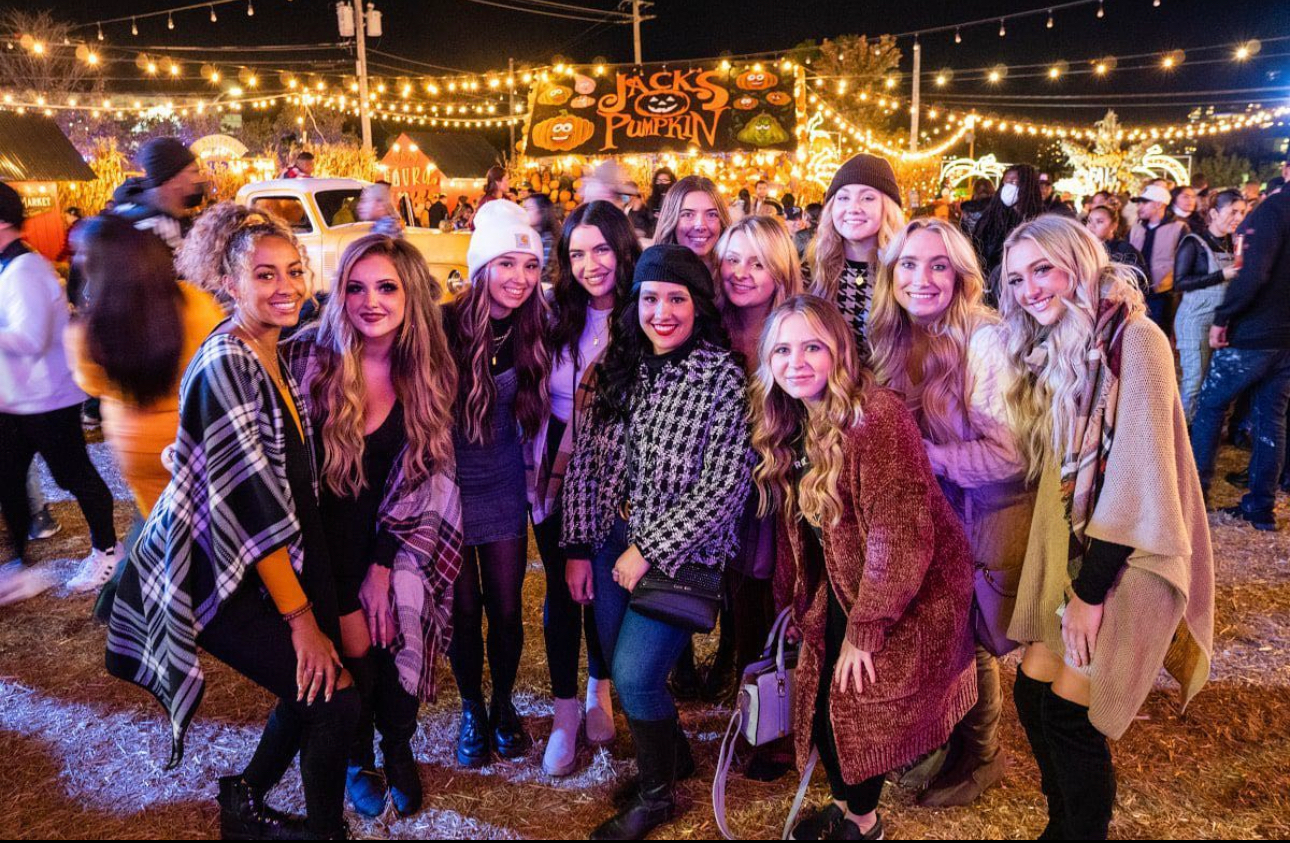 Group of friends posing at a nighttime outdoor party under string lights, smiling in festive outfits
