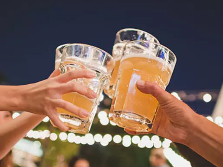 Hands clinking beer mugs at a night celebration with blurred lights in the background