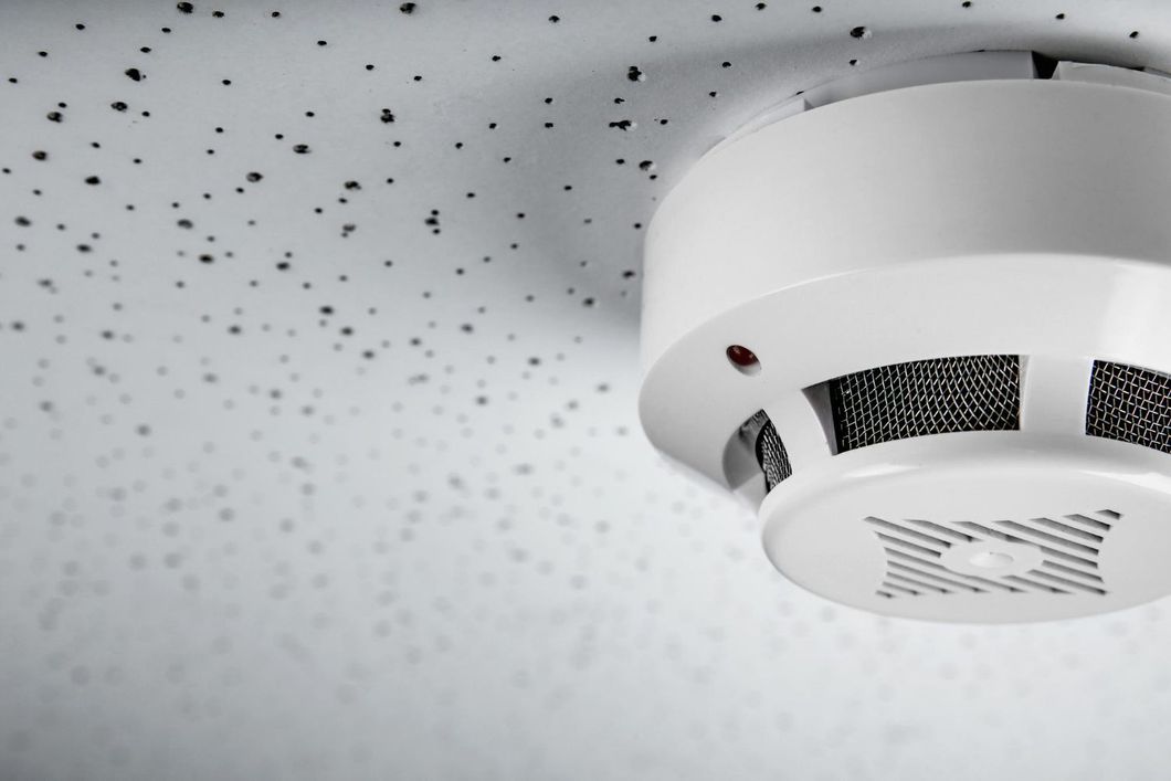 Ceiling-mounted white smoke detector against a speckled white ceiling