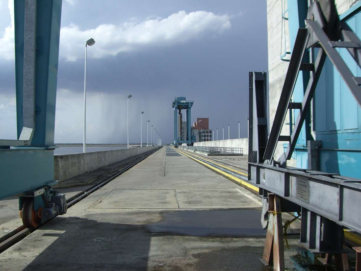 Empty industrial dock or bridge walkway under cloudy sky, with blue metal structures on both sides.