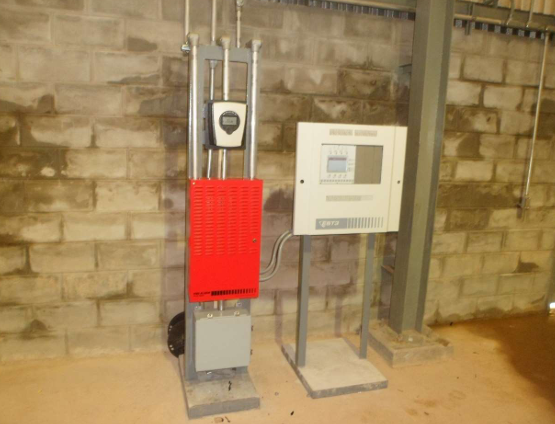 Two utility control panels on metal stands against a stone wall, one red and one white.