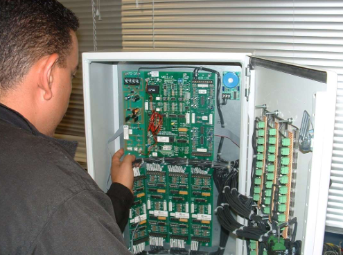 Technician inspecting an open electrical control panel with circuit boards and wiring.